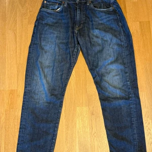 Levi's 502 mörkblå jeans W30 L30 - Snygga Levi's 502 jeans i mörkblå tvätt med klassisk femficksdesign och bruna sömmar. Modellen har rak passform och normal midja, tillverkade i slitstarkt jeanstyg. Perfekta för dig som gillar en tidlös och avslappnad stil.