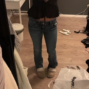 Blå lågmidjade bootcut jeans - Säljer ett par blå jeans med låg midja och bootcut-snitt. Jeansen har klassiska fem fickor, snygga sömmar och en cool tvätt som ger dem en vintage vibe. Passformen är normal och materialet är slitstarkt denim. Perfekta för dig som gillar retrostilen och vill ha ett par jeans som sticker ut.