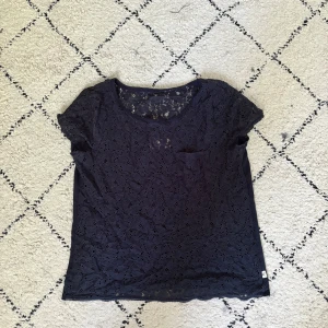 Mörkblå spetsblus från Hollister - Snygg mörkblå blus från Hollister i storlek S. Toppen har korta ärmar och är gjord i bomull med spetsdetaljer framtill och upptill på ryggen. Rund halsringning och liten bröstficka. 