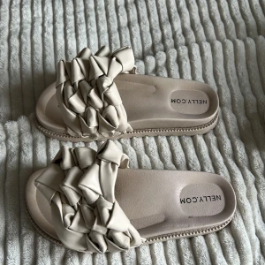 Beige sandaler med flätad rem från Nelly - Säljer ett par beige sandaler från Nelly med breda, flätade remmar i syntetmaterial. Sulan är platt och har en rund tå.Storlek 38.💕💕