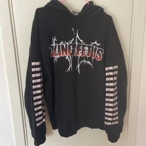 Svart Dying Fetus hoodie från Gildan - Säljer en svart hoodie från Gildan med Dying Fetus-tryck i rött och vitt på både fram- och baksida. Tröjan har huva, snörning och stor ficka framtill. Ärmarna har tryck med bandnamnet längs hela sidan. Materialet är en skön bomullsblandning.