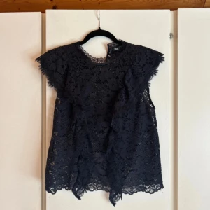 Svart spetsblus från Zara - Supersnygg svart blå blus från Zara med blommigt spetsmönster och korta ärmar. Blusen har rund hals och fina volangdetaljer längs axlarna. Perfekt för dig som gillar en romantisk och trendig look. Materialet är mjukt och luftigt.