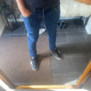 Blå skinny jeans från Nudie - Säljer ett par blå skinny jeans från Nudie med klassisk femficksdesign och snygga kontrastsömmar. Jeansen har en mörkblå ton, smal passform och är tillverkade i stretchig denim för extra komfort. Nudie-loggan syns på bakfickan och läderpatchen bak.