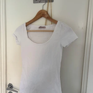 Vit t-shirt från Anna Field - Snygg vit t-shirt från Anna Field med rundad, djup halsringning och korta ärmar. Modellen är figurnära och passar perfekt till jeans eller kjol. Tillverkad i mjuk bomull som känns skön mot huden. Enkel och stilren design som funkar året runt.