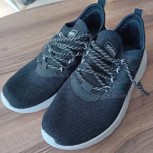 Svarta Adidas sneakers med vit sula - Snygga svarta Adidas sneakers med vit, platt sula och stickad ovandel i syntetmaterial. Skorna har svartvita snören och klassisk Adidas-logga på plösen. Perfekta för dig som gillar sportig stil och vill ha bekväma skor till vardags.