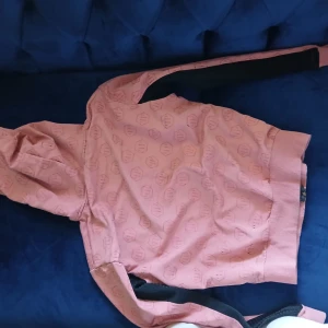 Rosa hoodie från Philipp Plein XXL - Säljer en rosa hoodie från Philipp Plein i storlek XXL men passar för S/M eftersom den är liten..Tröjan har ett all-over logomönster, svarta ribbade detaljer på ärmar och sidor, dragkedja framtill och huva med guldfärgade paljettdetaljer. Perfekt för dig som gillar streetwear med lyxig vibe.