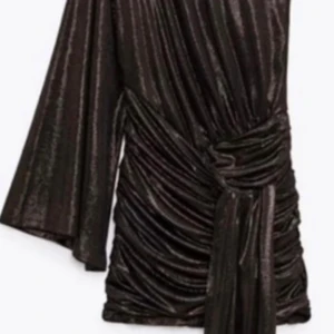 Glittrig guld från Zara - Snygg svart kortklänning från Zara med glittrigt tyg och omlott-design. Klänningen har en oneshoulder-look med en lång ärm och coola rynkade detaljer samt knyt i midjan. Perfekt för dig som vill sticka ut med en trendig och unik stil.