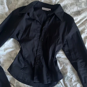 Helsvart figursydd skjorta - Denna är mer svart i verkligheten, materialet är mjukt och stretchigt! Storlek XS från Hennes Collection. Jag fraktar gärna - köparen står för frakten, annars hämtas skjortan upp i Tyresö/Globen 💞