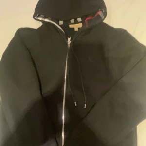 Svart vindjacka från Burberry M - Svart vindjacka från Burberry med klassiskt rutigt foder i svart, vitt och rött. Jätte bra skick knappt använd. Pris kan diskuteras!