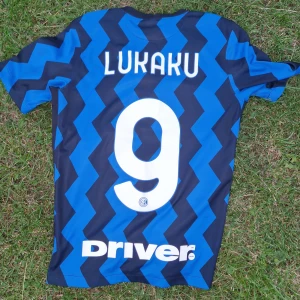 Inter Milan Lukaku #9 matchtröja Nike L - Säljer en officiell Inter Milan fotbollströja med Lukaku och nummer 9 på ryggen från 20/21 säsongen. Tröjan är blå och svart med zigzag-randigt mönster, har korta ärmar och är gjord i 100% återvunnen polyester. Pirelli-logga på bröstet och broderat Inter-emblem med stjärna. 