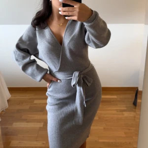 Grå omlottklänning med bälte - Snygg grå ribbad omlottklänning med v-ringning och knytbälte i midjan. Klänningen har långa ärmar och är knälång, vilket ger en chill men ändå stilren vibe. Perfekt för dig som gillar enkel men trendig design. Vädligt skön och sitter väldigt fint. Pris kan diskuteras. Inga fläckar.