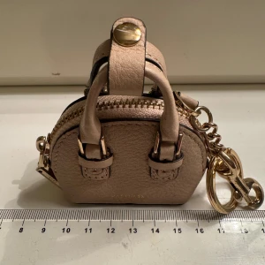 Mini handväska som nyckelring  - Supergullig mini handväska med guldfärgade detaljer och dragkedja. Beige/rosa. Som nyckelring eller accessoar att hänga på väskan. Får plats med lite mynt eller piller. Hämtas på Hägerstensåsen om du vill. 