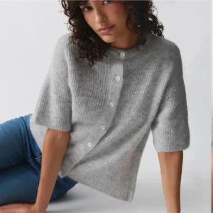 Grå ribbad kofta från Gina Tricot - ny med prislappen kvar!Supermysig grå ribbad kofta från Gina Tricot med rund hals och korta ärmar. Koftan har knappar framtill och är tillverkad i en mjuk stickad kvalitet som känns lyxig. Perfekt för lager-på-lager och chill outfits.