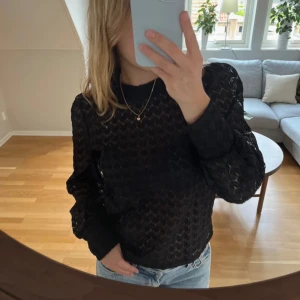 Svart spetsblus från Nelly - Supersnygg svart blus från Nelly med genombruten spets och diskret mönster. Blusen har långa ärmar, hög hals och knäppning bak i nacken. Använd en gång och är som ny💛
