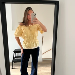 Gul offshoulder blus med spetsdetaljer - Söt gul blus med offshoulder och knytning framtill. Har en fläck i fram (sista bilden) men inget som jag lagt märke till när jag använt den eftersom knytningen hänger över! Står ingen storlek och det är något gammalt märke. Skulle uppskatta den XS-L eftersom den är väldigt stretchig