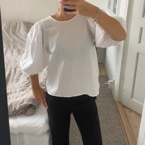 Vit blus med puffärmar och knyt - Säljer en vit blus med rund hals och puffiga trekvartsärmar. Blusen har ett knyt i nacken och är gjord i ett lätt bomullstyg. 