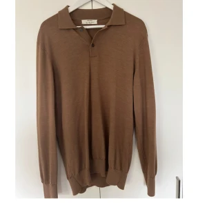 Brun pikétröja i ull från Zara - Snygg brun pikétröja från zara i mjuk ull. Tröjan har klassisk krage, två knappar vid halsen och långa ärmar med ribbade muddar. Perfekt för dig som gillar stilrena och enkla plagg med premiumkänsla.