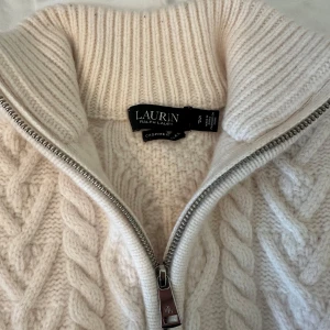 Vit kabelstickad från Ralph Lauren - Säljer en vit kabelstickad tröja från Ralph Lauren i mjuk cashmere. Tröjan har en hög ribbad krage och half zip-dragkedja framtill. Aldrig använd så inga märken