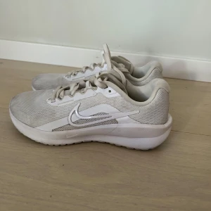 Vita Nike Running sneakers - Fräscha vita Nike Running sneakers med mesh-ovandel och klassisk swoosh på sidan. Skorna har snörning och platt sula för skön komfort. Perfekta för dig som gillar sportig stil och vill ha lätta skor till träning eller häng. Snyggt och cleant utseende som funkar till det mesta.