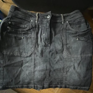 Svart jeanskjol med fickor - Snygg svart jeanskjol med fallande stjärnor och "kontrastsömmar". Klassiska fem fickor, både fram och bak.  Kjolen har knapp och dragkedja framtill. Den har en rak passform som ger en cool och avslappnad vibe.