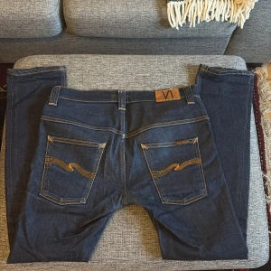 Nudie Jeans Tape Ted blå jeans W32 L32 - Säljer ett par mörkblå Tape Ted jeans från Nudie Jeans i storlek W32 L32. Jeansen har klassisk femficksdesign, kontrastsömmar och är tillverkade i 99% ekologisk bomull och 1% elastan för lite stretch. Snyggt broderade bakfickor och rak/slim passform