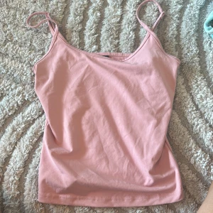 Ljusrosa linnetopp med smala axelband - Säljer en ljusrosa linnetopp med smala axelband och enkel, rak passform. Toppen är gjord i mjuk bomull och har en clean look utan mönster eller detaljer. Perfekt för dig som gillar minimalistisk stil och vill ha något bekvämt och snyggt.