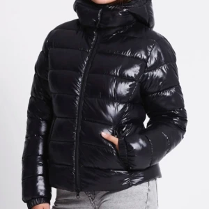 Svart jacka  - Svart, glansig pufferjacka från 157 i storlek XS. Jackan har en luva, dragkedja framtill och två sidofickor. Perfekt till vintern. OBS! den har en liten smink fläck uppe i luvan men ska tvätta och se om det går bort.