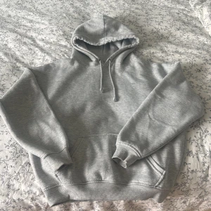 Grå hoodie från Bik Bok XS - Säljer en enkel och snygg grå hoodie från Bik Bok i storlek XS. Tröjan har huva med snörning, stor magficka och är tillverkad i mjuk blandning av polyester och bomull. Perfekt för chill dagar eller när du vill ha en clean look.