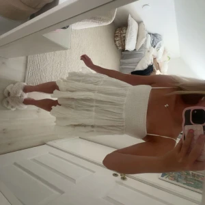 Vit kort sommarklänning med volang - Supersöt vit klänning med smockad överdel och tunna axelband. Kjolen är kort och har flera lager med volanger som ger en fluffig och romantisk look. Perfekt för varma dagar och har en lätt, luftig känsla. Passar dig som gillar en feminin och chill stil. Banden är något gulnade men annars är den i bra skick! 