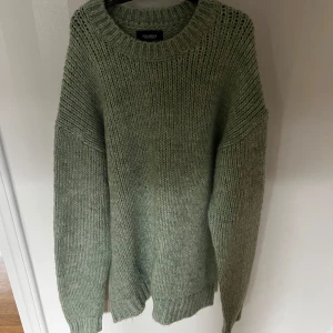 Grön stickad tröja Pull&Bear M - Mysig grön stickad tröja från Pull&Bear i storlek M. Tröjan har en loose passform, grovstickad struktur och rund hals. Perfekt för kyliga dagar och enkel att matcha med jeans eller kjol. Färgen är en mjuk grön ton som ger en chill vibe.