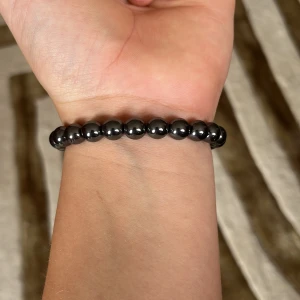 Svart pärlarmband med glans - Snyggt svart armband med glansiga, runda pärlor som sitter på en elastisk tråd. Perfekt för dig som gillar minimalistisk och stilren design. Pärlorna har en cool metallic-look som ger armbandet en modern vibe.