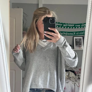 Grå stickad v-ringad tröja - Mysig grå stickad tröja med v-ringad hals och långa ärmar. Tröjan har en loose passform och ribbade muddar vid ärmslut och nederkant. Perfekt att slänga på över en t-shirt för en chill och avslappnad look. säljer för den ej kommet till användning. stor för mej som har xs