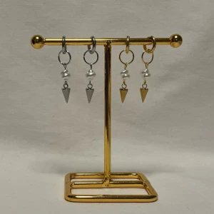 Örhängen med pärlor och spetsiga hängen - Coola örhängen i både silver och guld med runda ringar, vita pärlor och spetsiga konformade hängen. Perfekt för dig som gillar edgy detaljer och vill sticka ut. Säljs som två par, ett i silver och ett i guld, båda med vita pärlor och metallhängen.