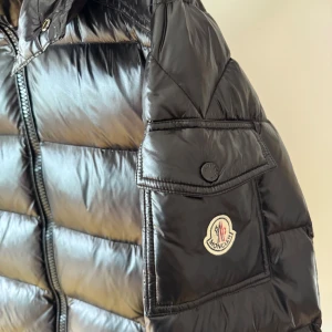 Svart Moncler pufferjacka med huva - Svart pufferjacka från Moncler, huva och dragkedja framtill. Jackan har två fickor med dragkedja. Bra skick. Storlek 3, liknar medium. 