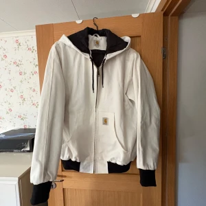 Vit Carhartt jacka - Säljer en clean vit jacka från Carhartt med svart huva och muddar. Som ny! Jackan har dragkedja framtill, snörning i huvan och två fickor. Materialet är slitstark bomull och passformen är loose. Perfekt för dig som gillar streetwear och vill sticka ut. Nypris runt 2800. MITT PRIS GÅR ATT DISKUTERA SÅ BARA ATT SKRIVA☺️