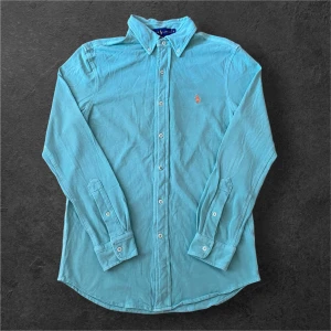 Ljusblå skjorta från Ralph Lauren S - Snygg ljusblå skjorta från Ralph Lauren i featherweight mesh. Klassisk modell med knappar hela vägen, button down-krage och broderad logga på bröstet. Perfekt för dig som gillar stilrena och bekväma plagg.