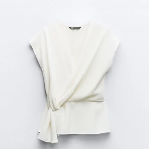 Vit omlottopp från Zara - Tryck inte på köp nu! Stilren vit omlottopp från Zara med knyt i sidan och v-ringad design. Toppen är ärmlös och har en elegant, enkel look som passar perfekt till jeans eller kjol. Lätt och luftig känsla, perfekt för varmare dagar. Toppen är endast testad, aldrig använd.