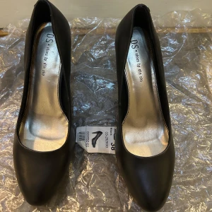 Svarta pumps från Din Sko, storlek 38 - Klassiska svarta pumps från Din Sko med spetsig tå och elegant låg klack (10 cm). Skorna har en stilren design i syntetmaterial och en metallicfärgad innersula som ger en snygg kontrast. Perfekta för dig som gillar en tidlös och clean look. Endast använd en gång. 