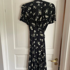 Blommig långklänning från & Other Stories - Supersnygg svart långklänning från & Other Stories med vitt blommönster. Klänningen har omlottmodell, v-ringning och korta, fladdriga ärmar. Perfekt för dig som gillar romantisk och flowy stil. Materialet känns lätt och luftigt.