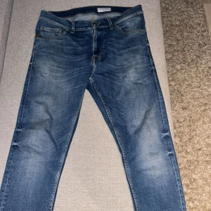 Blå jeans från Tiger of Sweden - Snygga blå jeans från Tiger of Sweden i modellen Evolve. Klassisk femficksdesign med mellanblå tvätt och subtila slitningar. Jeansen har raka ben och normal passform, tillverkade i bomull med snygga kontrastsömmar.