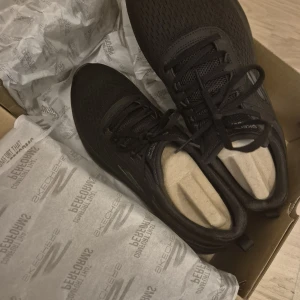 Svarta Skechers GOwalk sneakers - Säljer ett par svarta Skechers GOwalk Arch Fit sneakers med mesh-ovandel och snörning. Skorna har en chunky, platt sula och diskret S-logga på sidan. Perfekta för dig som vill ha bekväma och stilrena skor till vardagen. Luftig och sportig känsla.