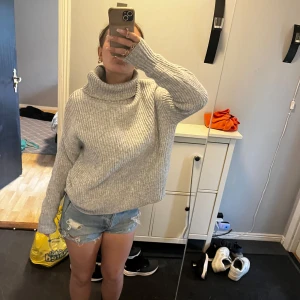 Grå stickad polotröja - Mysig grå stickad polotröja med oversized passform och ribbad struktur. Tröjan har en hög, vikt krage och långa ärmar, perfekt för kyliga dagar. Köpt utomlands och är jätte musik tills höst/vinter🥰🥰🥰 storlek M