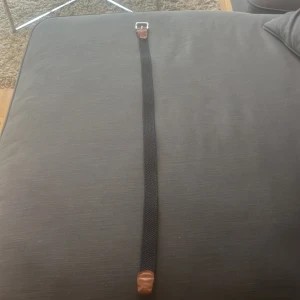 Mörkblå flätat bälte från Jack & Jones - Snyggt svart flätat bälte från Jack & Jones med detaljer i brunt skinn och silvrigt spänne. Bältet har en klassisk design med vävd struktur och passar perfekt till jeans eller chinos. Längd 90 cm enligt märkning på lädret.