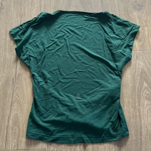 Mörkgrön kortärmad topp i bomull - En enkel och stilren mörkgrön topp från Zara. Modellen är kortärmad med rund halsringning och tillverkad i mjuk bomull. Perfekt att matcha med jeans eller kjol för en clean look. Öppen rygg.