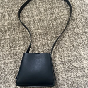 Svart axelväska  - Minimalistisk svart axelväska i slätt skinn med bred axelrem och innerfack med dragkedja. Justerbart axelband och går att ta bort helt och ha som handväska. Finns mycket plats att förvara saker i väskan, den är stilren och passar till allt. Från Gina tricot, aldrig använd någonsin, helt nyskick och noll defekter. 