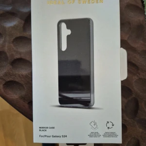 Svart Mirror Case Galaxy S24 iDeal - Snyggt svart spegel-fodral från iDeal of Sweden till Galaxy S24. Skalets baksida har en spegel-look och är tillverkat av återvunnet material. Slimmad design med öppning för kameran och diskret logga längst ner.