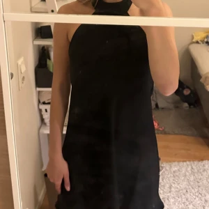 Svart kort klänning med öppen rygg - Säljer en svart kort klänning med halterneck och helt öppen rygg. Klänningen har en stilren och enkel design, är ärmlös och har en rak passform. Perfekt för dig som vill ha en clean och snygg look. Materialet känns mjukt och följsamt.