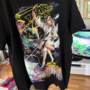 Star Wars t-shirt från H&M  - Svarte t-shirt från H&M med stor färgglad Star Wars-tryck framtill. Motivet visar klassiska karaktärer och texten 'May the force be with you!'. T-shirten har rund hals och korta ärmar, tillverkad i mjuk bomull. Perfekt för dig som älskar retro och sci-fi. Storlek L aldrig använd. 