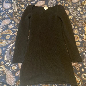 Svart stickad klänning - En svart stickad klänning med lång ärm och rundad hals. Klänningen har en ribbad struktur och sitter figurnära, perfekt för dig som gillar en enkel men snygg look. Passar till boots eller sneakers för en chill vibe.