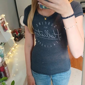 Mörkblå t-shirt från Hollister - Snygg mörkblå t-shirt från Hollister.  Klassisk rund halsringning och korta ärmar. Bra passform runt midjan och mjukt material, perfekt till jeans eller shorts. Stilren och enkel design med en avslappnad vibe. Har ett litet hål framtill som man kan se på bilden